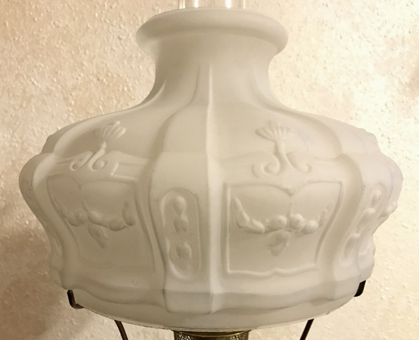Close-up of a white frosted glass lampshade with embossed floral and swirl designs.