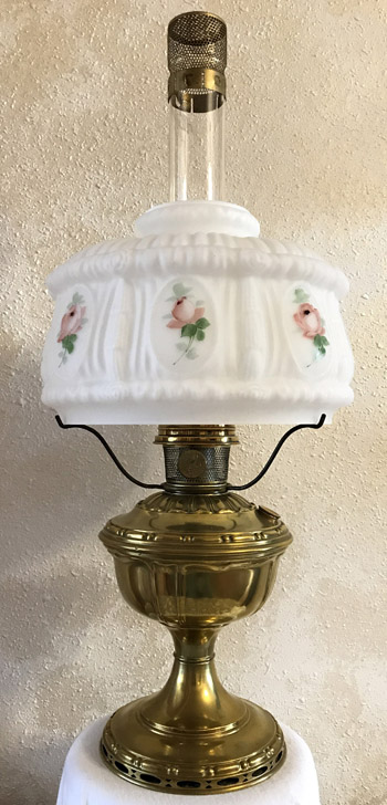 Vintage brass oil lamp with glass chimney and white floral milk glass shade.