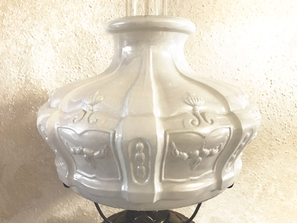 Glossy porcelain lamp shade with embossed floral and butterfly decorations on a beige wall background.