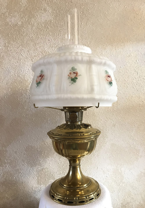 Vintage brass oil lamp with white glass shade decorated with pink roses and green leaves.