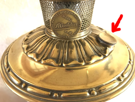 Close-up of a polished brass Aladdin lamp base with a round knob and perforated burner.
