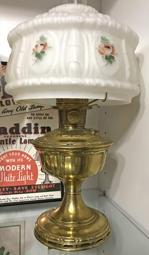 Vintage brass oil lamp with frosted glass shade decorated with pink roses and green leaves.