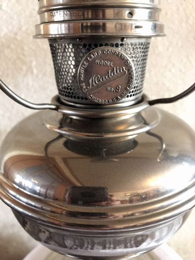 Close-up of a shiny metal Aladdin model 9 lantern burner with a mesh chimney.