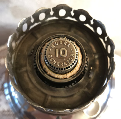 Close-up of a metal burner cap labeled Model 10 Generator on an oil lamp burner.