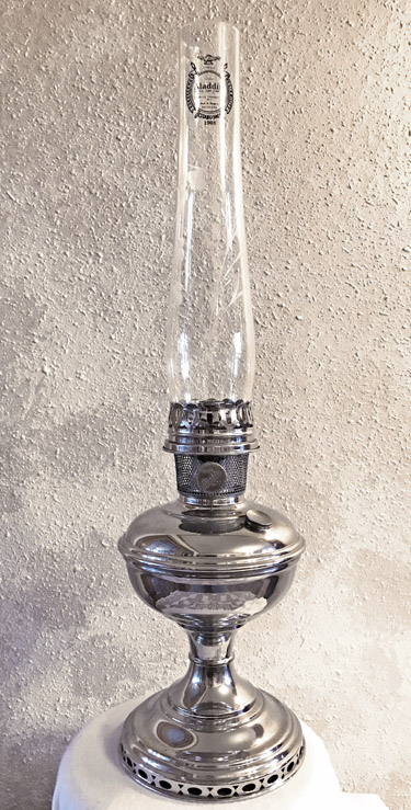 Shiny silver vintage oil lamp with tall clear glass chimney on a textured wall background.