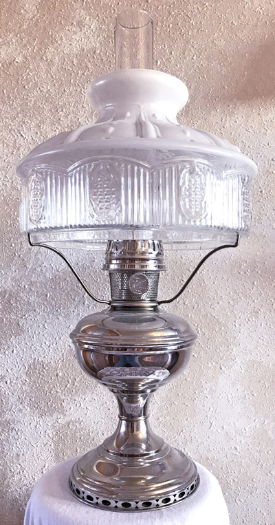 Vintage silver oil lamp with clear glass middle and white decorative top on white cloth.