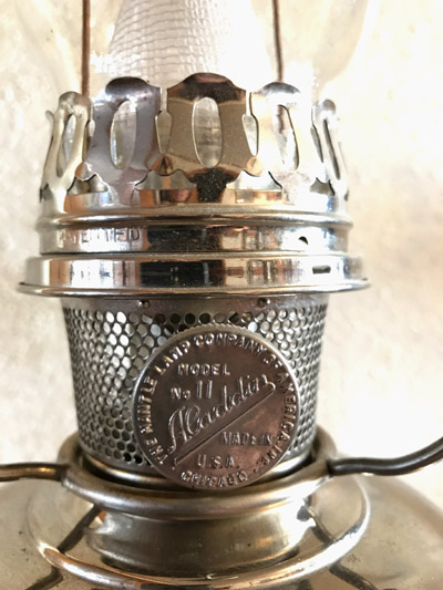 Close-up of a metal Aladdin lamp burner with perforated chamber and model details on a circular plate.