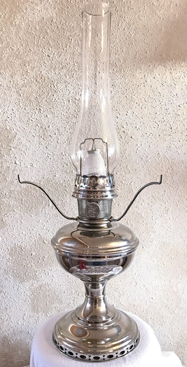 Vintage silver oil lamp with glass chimney and a wick holder, set against textured wall.
