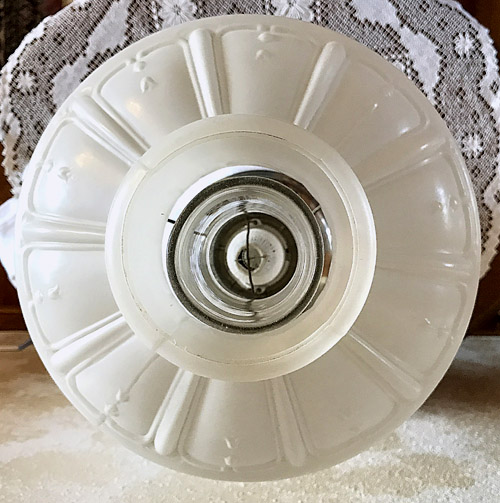 Close-up view of a vintage frosted glass lampshade with decorative ridges and a hanging lace backdrop.