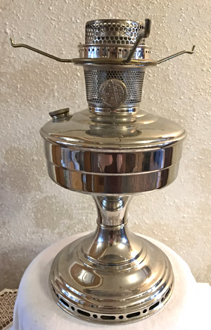 Polished silver vintage kerosene oil lamp on a white surface against a textured wall.