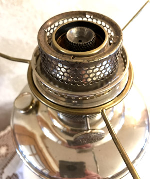 Close-up of a shiny metal vintage oil lantern burner with mesh and brass details.