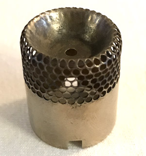 Small metal cylinder with honeycomb-patterned top and a hole in the center, placed on a white surface.