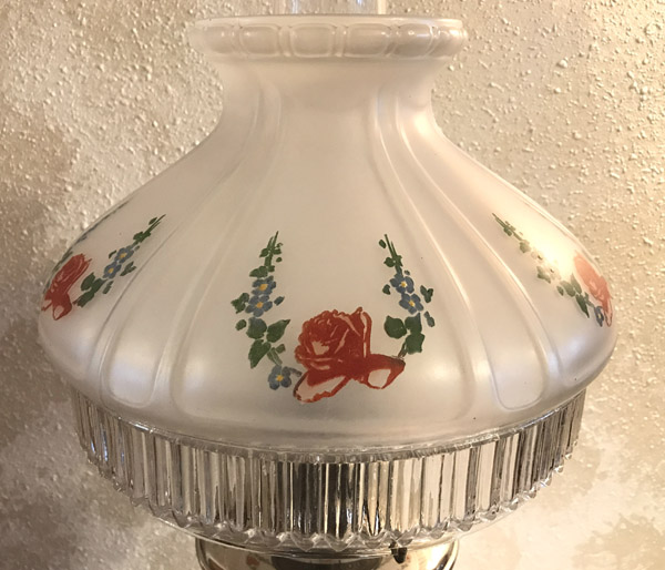Vintage frosted glass lamp shade with red rose and blue floral painted patterns on textured wall.