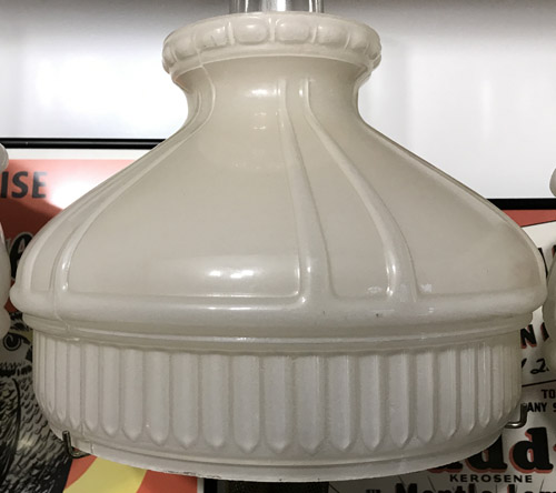 Close-up of a vintage white glass lamp shade with ribbed and paneled design.