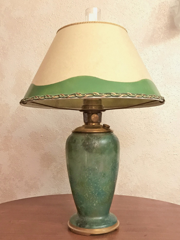 Table lamp with a green ceramic base and beige lampshade with green trim on a wooden surface.
