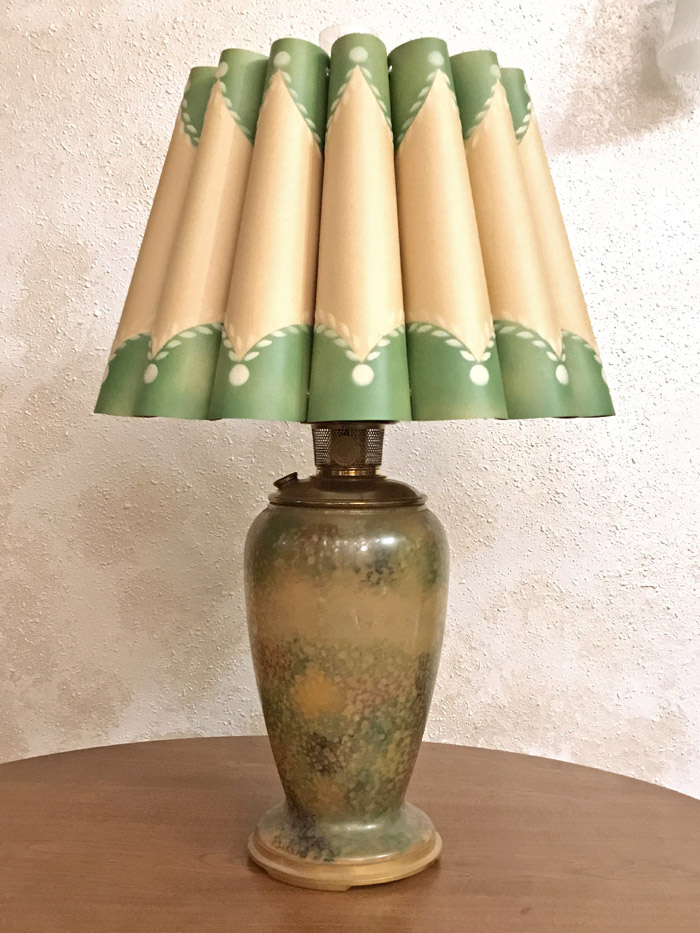 Vintage table lamp with patterned green and tan pleated lampshade on a mottled ceramic base.