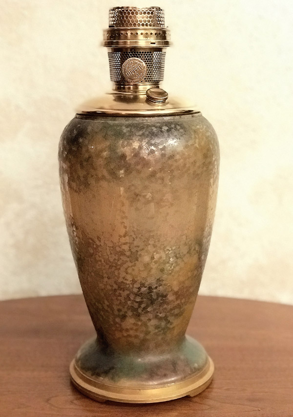 Vintage brass oil lamp with hammered texture on a wooden surface against a beige background.