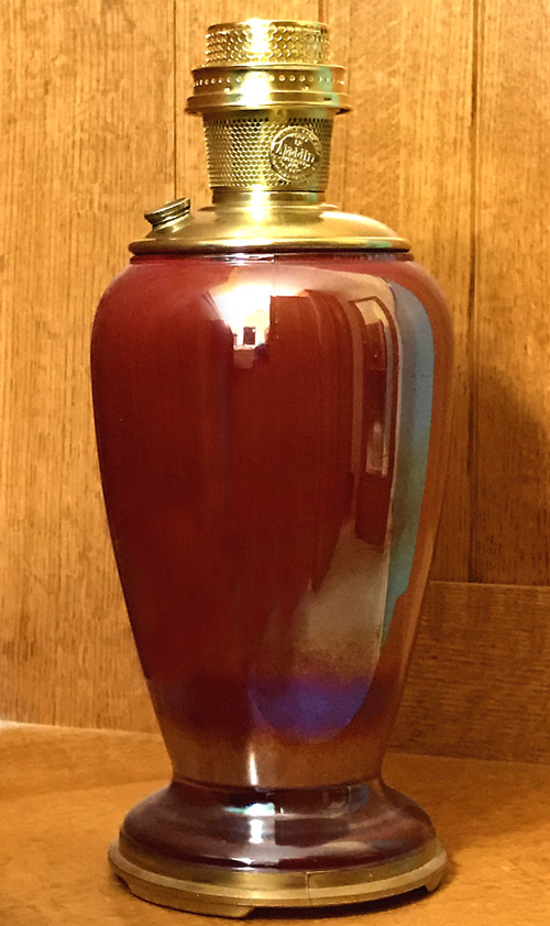 Red ceramic table lamp with shiny brass top and base on a wooden surface against wood paneling.