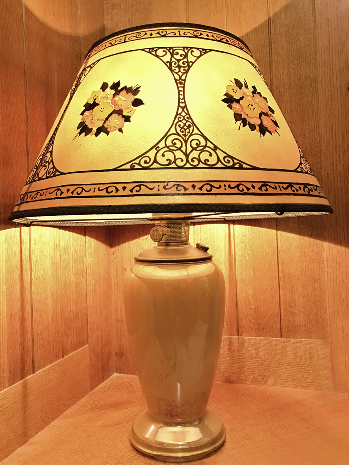 Vintage table lamp with floral-patterned shade on a wooden corner surface and wood-paneled walls.