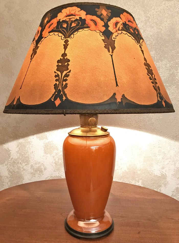 Orange ceramic table lamp with a floral-patterned beige and brown lampshade on a wooden surface.