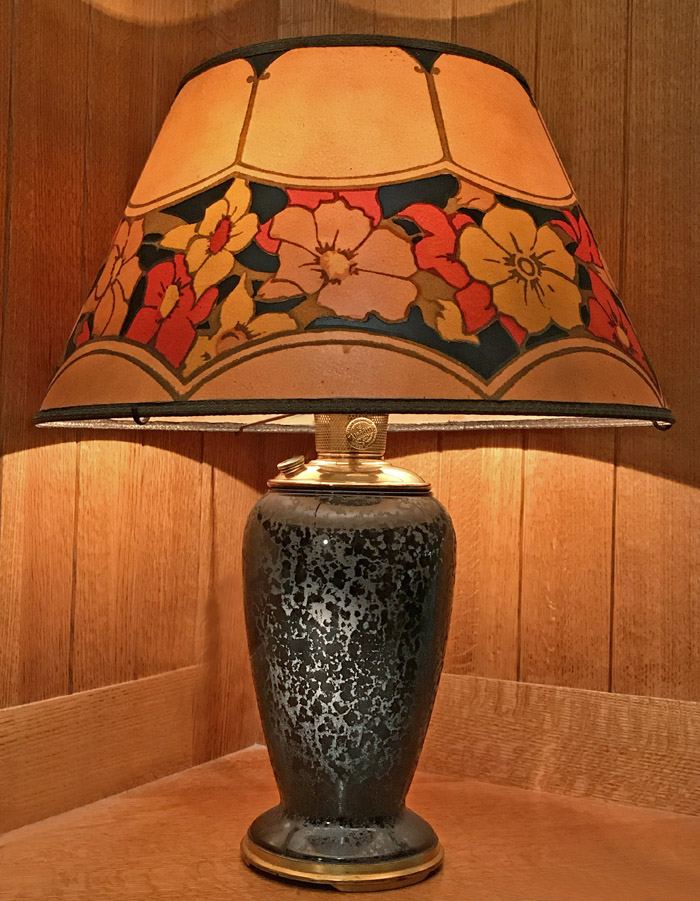 Table lamp with a black speckled ceramic base and a colorful floral-patterned shade on a wood surface.