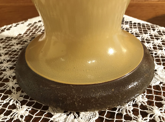 Close-up of a yellow vase base with a dark brown foot on a white crocheted cloth.