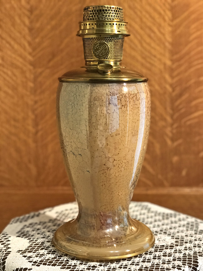 Antique brass and ceramic oil lamp with perforated brass burner on a lace doily.
