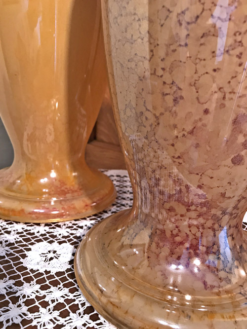 Close-up of two peach ceramic vases with marbled texture placed on white lace cloth.