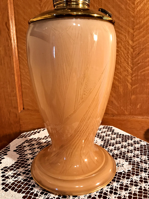 Tan ceramic vase with etched leaf patterns on a lace doily on a wooden surface.