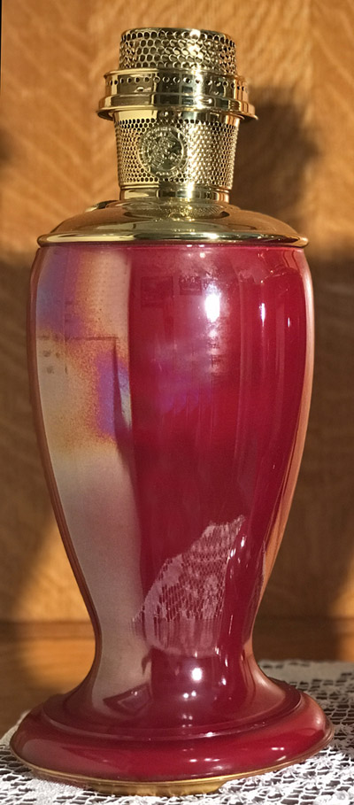 Glossy red ceramic lamp with shiny gold metal burner on top against wooden background.