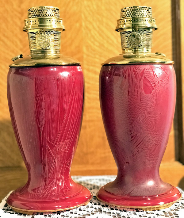 Pair of red vintage oil lamps with brass tops sitting on a lace doily on a wooden surface.