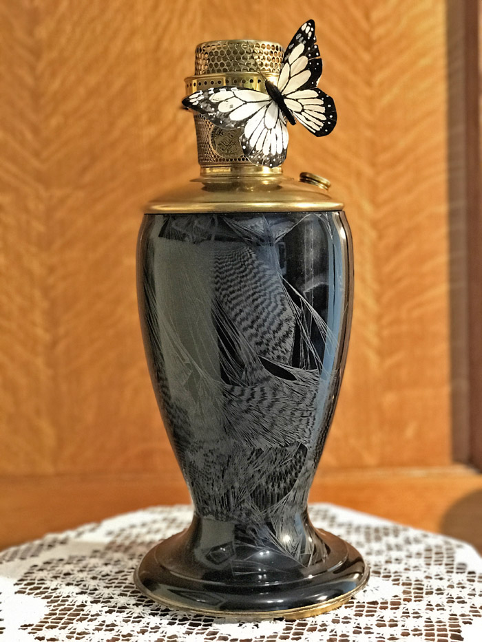 Black decorative vase with etched bird designs and a gold top, adorned with a white and black butterfly.