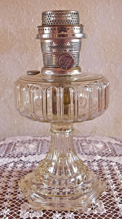 Vintage glass oil lamp with decorative base and metal burner on a lace tablecloth.