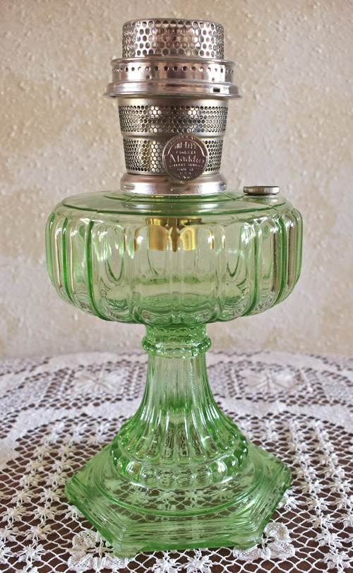 Green vintage glass oil lamp with silver metal burner on a lace tablecloth.