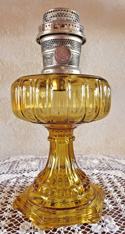 Amber glass oil lamp with ornate base and metal burner on a lace tablecloth.