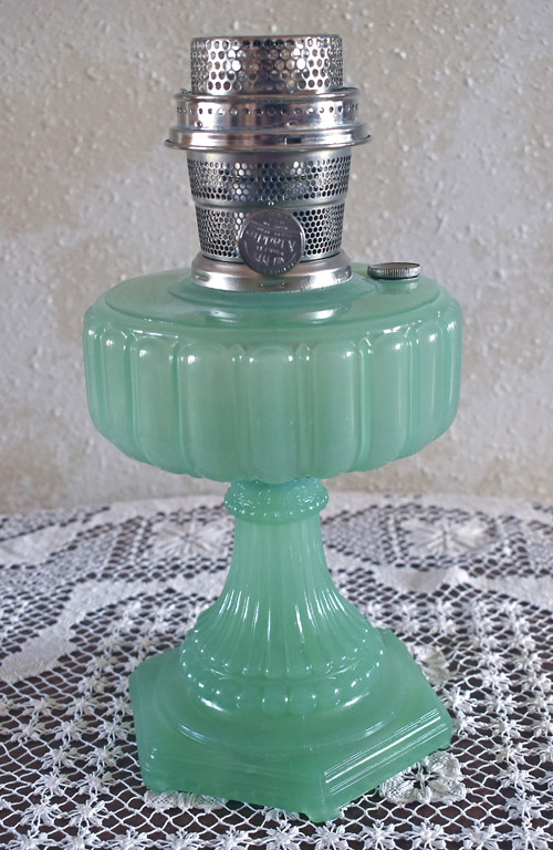 Antique green glass oil lamp with a silver metal burner on a lace tablecloth.