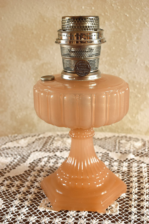 Vintage pink glass Aladdin oil lamp with silver metal burner on lace tablecloth.