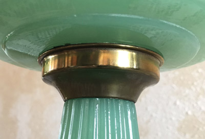Close-up of a green ribbed glass column with a brass Corinthian connector under a glass dish.