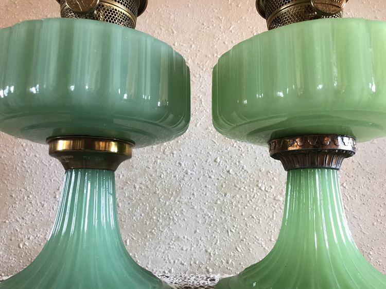 Close-up of two green glass lamp bases with metallic connectors on a textured wall background.