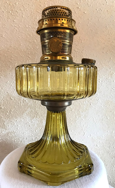 Vintage light amber glass oil lamp with brass burner and fluted base on white cloth.