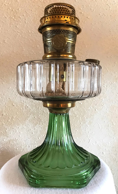 Antique oil lamp with a green glass base and clear ribbed glass font and a brass burner.