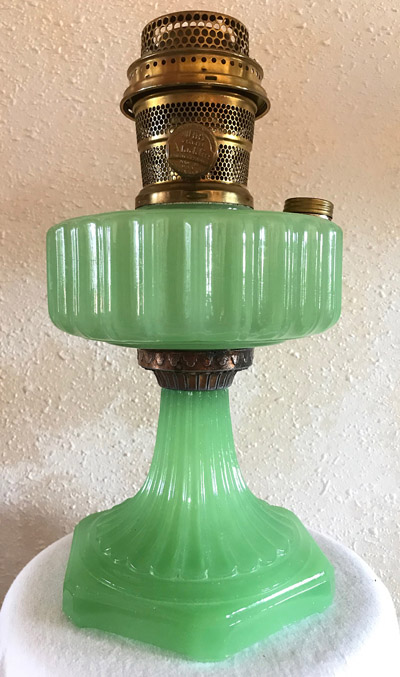 Green glass vintage oil lamp with ribbed design and brass burner on a white surface.