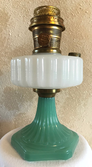 Vintage kerosene lamp with green glass base, white ribbed glass fuel reservoir, and brass burner top.
