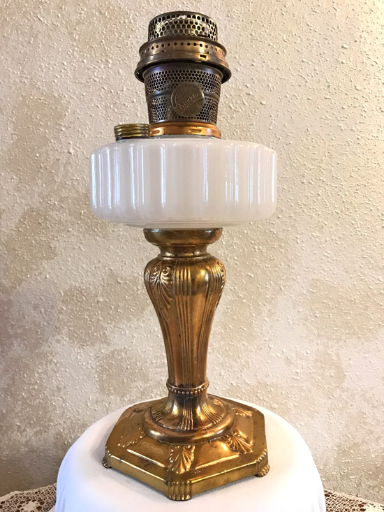 Antique brass oil lamp with white glass font and ornate base on white cloth.