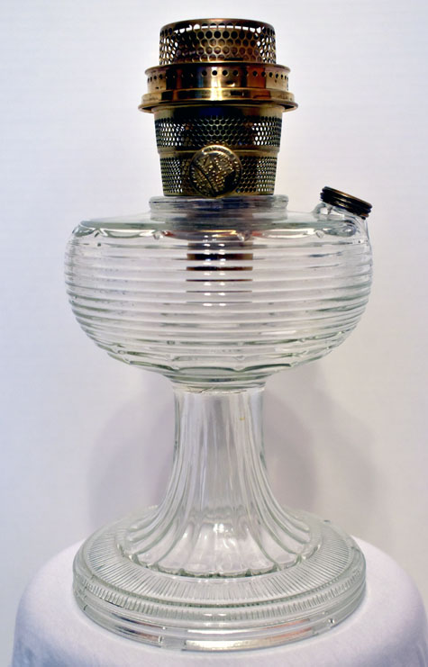 Clear ribbed glass oil lamp with brass burner on a white surface against a plain background.