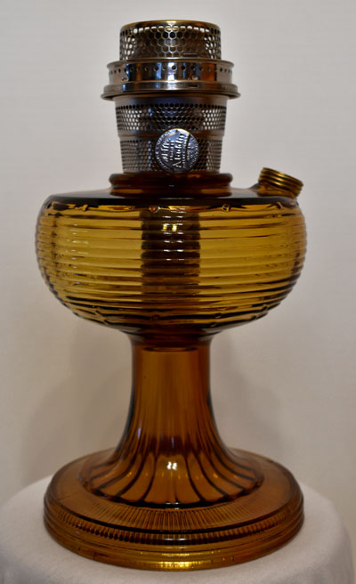 Vintage amber glass oil lamp with a metal burner and wick adjustment knob.