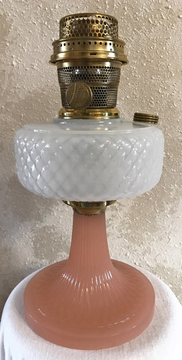 Vintage oil lamp with a pink glass base, white quilted glass reservoir, and brass burner.