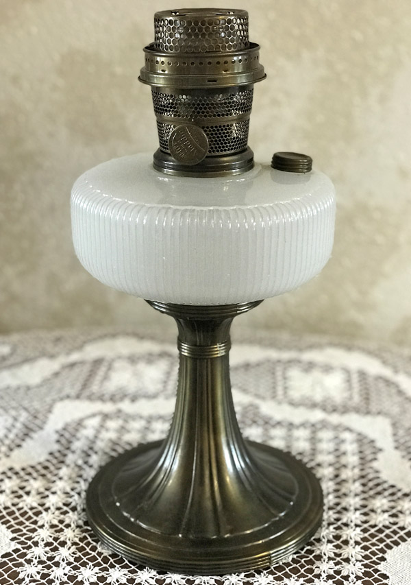 Antique brass oil lamp with white ribbed glass font on a lace tablecloth.