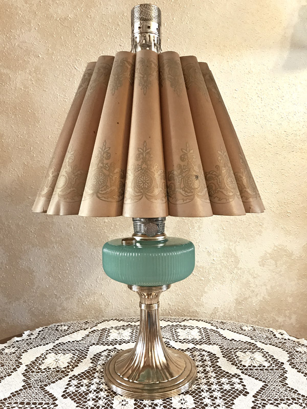 Vintage table lamp with a pleated beige shade and a ribbed green glass base on a lace cloth.