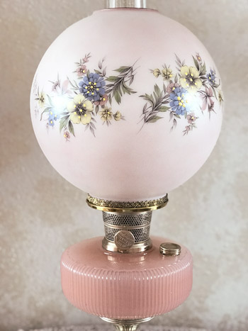 Vintage pink glass oil lamp with floral design on round globe shade and ribbed base.